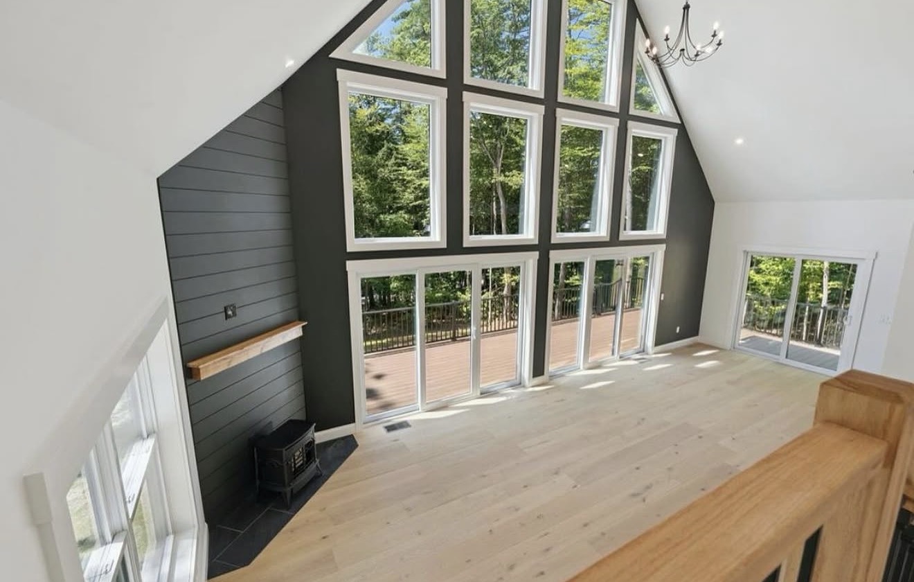 Great room with two-story window wall, dark shiplap accent, and wood stove in a custom New Hampshire home