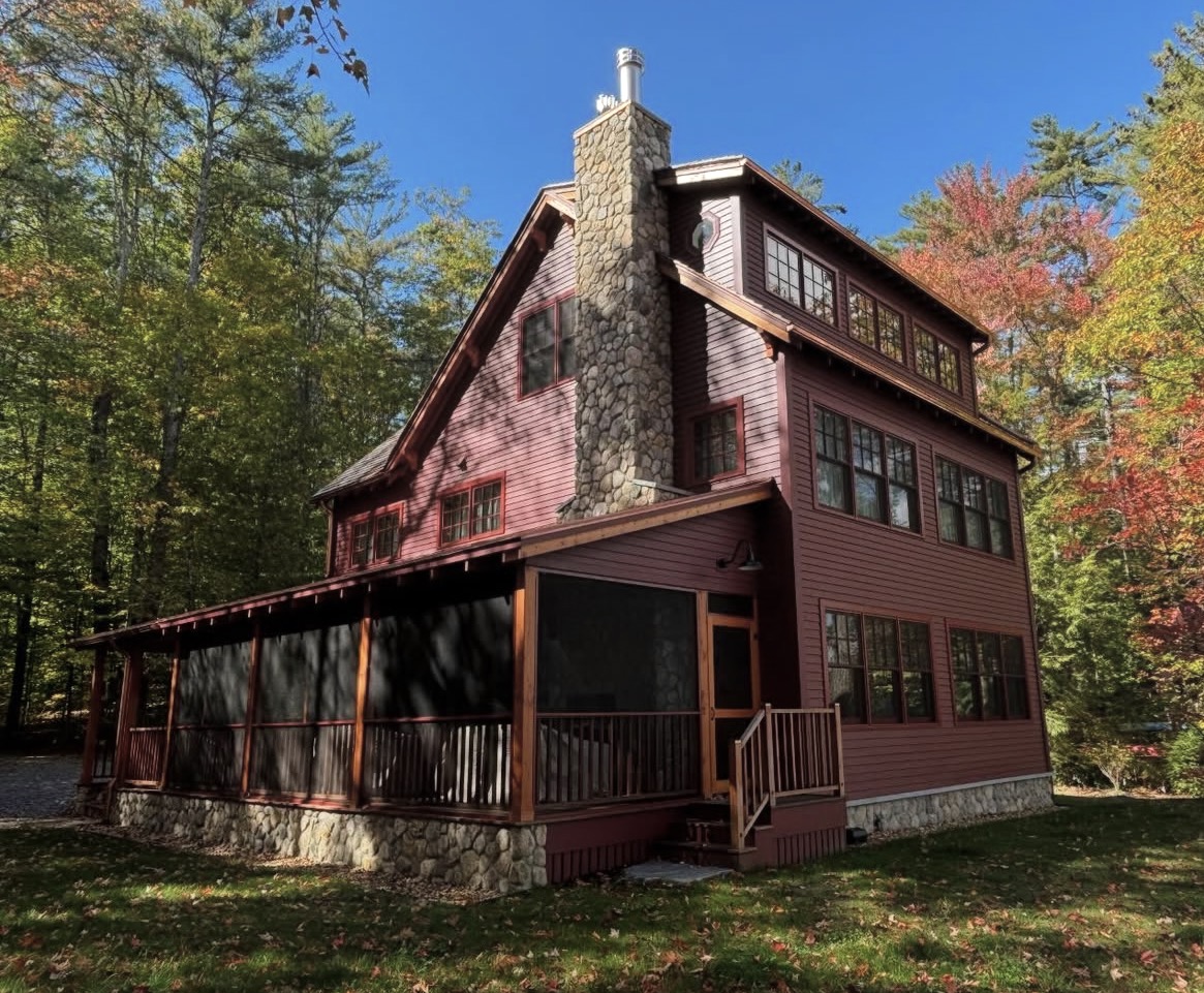 Deep-red rustic custom home with stone chimney and screened porch in the NH Lakes Region, fall foliage