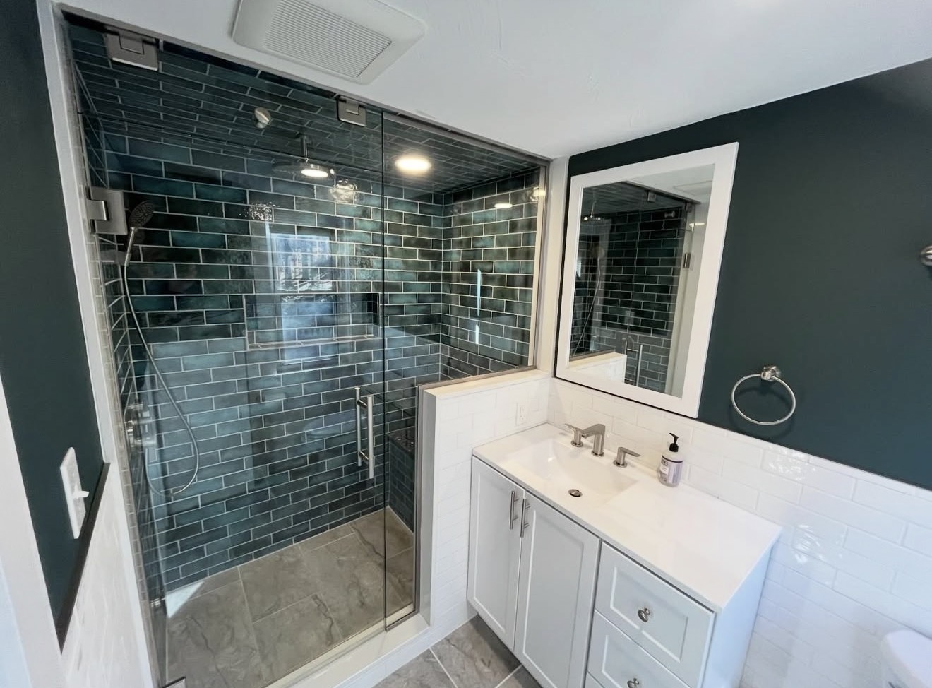 Bathroom remodel with dark-teal subway tile shower, glass door, and rainfall shower head in New Hampshire